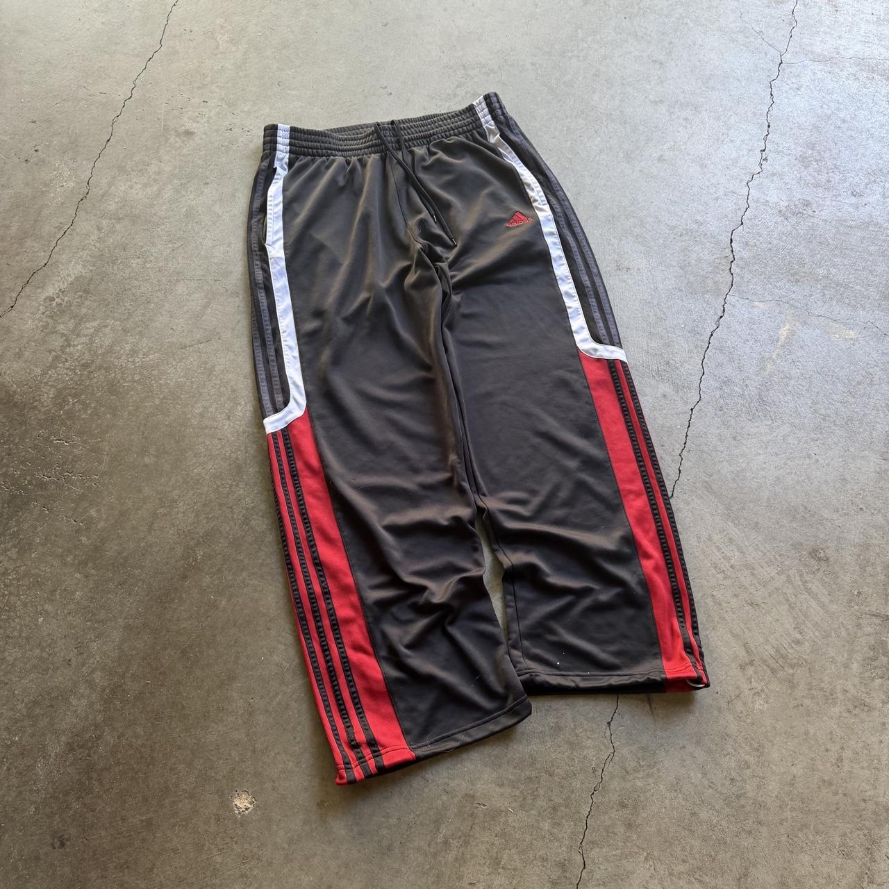 Black, white, and red Adidas track pants laid on concrete