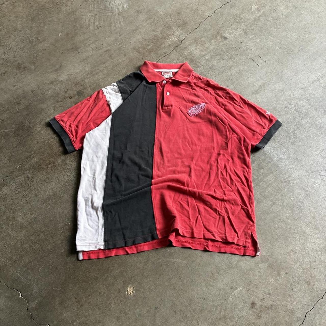 Red, black, and white Detroit Red Wings polo laid on concrete