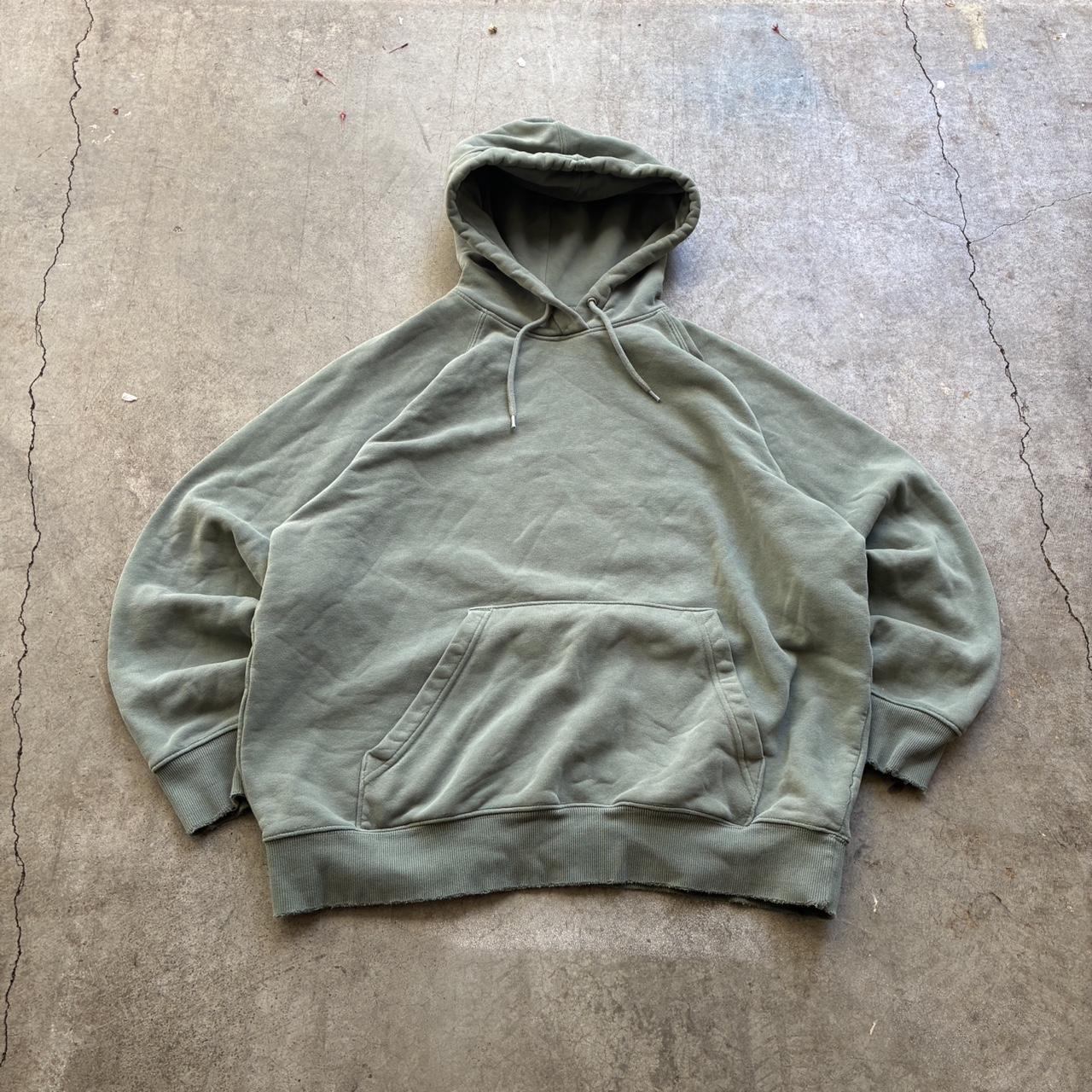 Sage green pullover hoodie laid on concrete